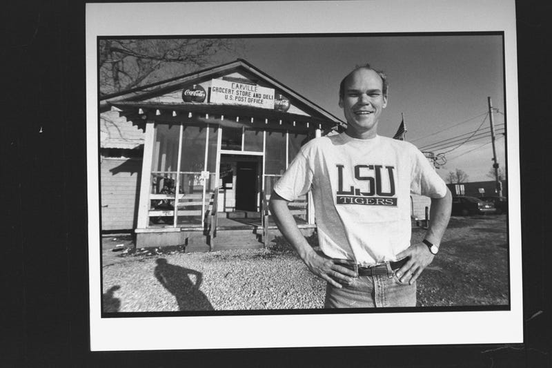 James Carville posing in LSU Tigers t-shirt as he stands in front of Carville Post Office & grocery store.
