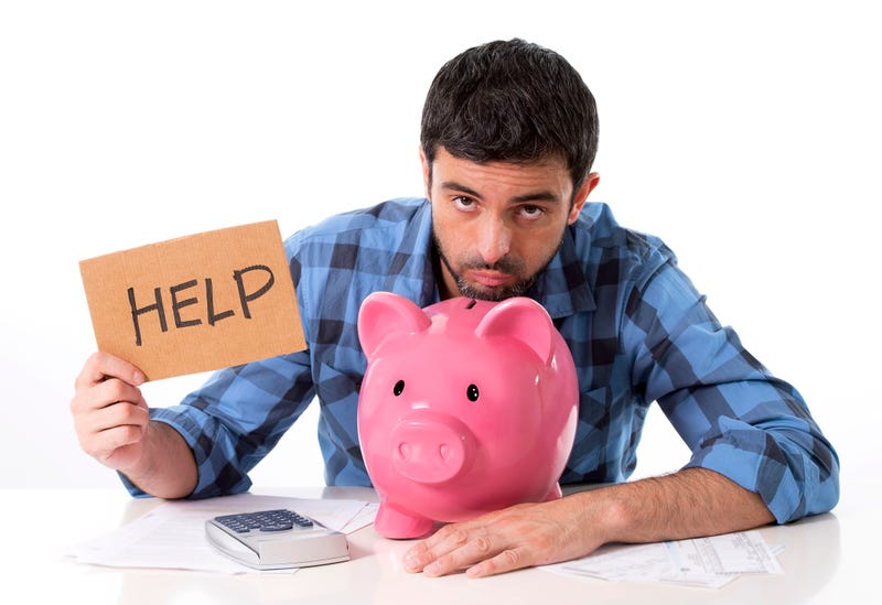Man with his head resting on a large pink piggy bank holding a sign that reads "help."