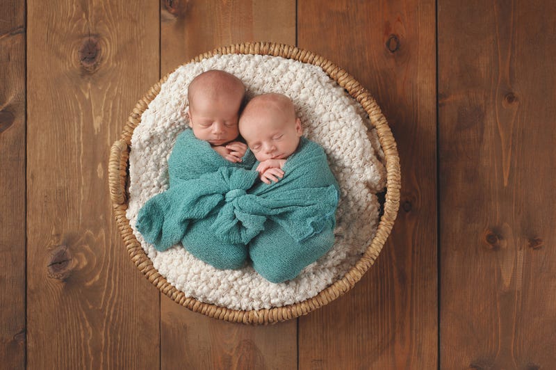 twin baby boys swaddled in a turquoise blue wrap and sleeping in a wicker basket