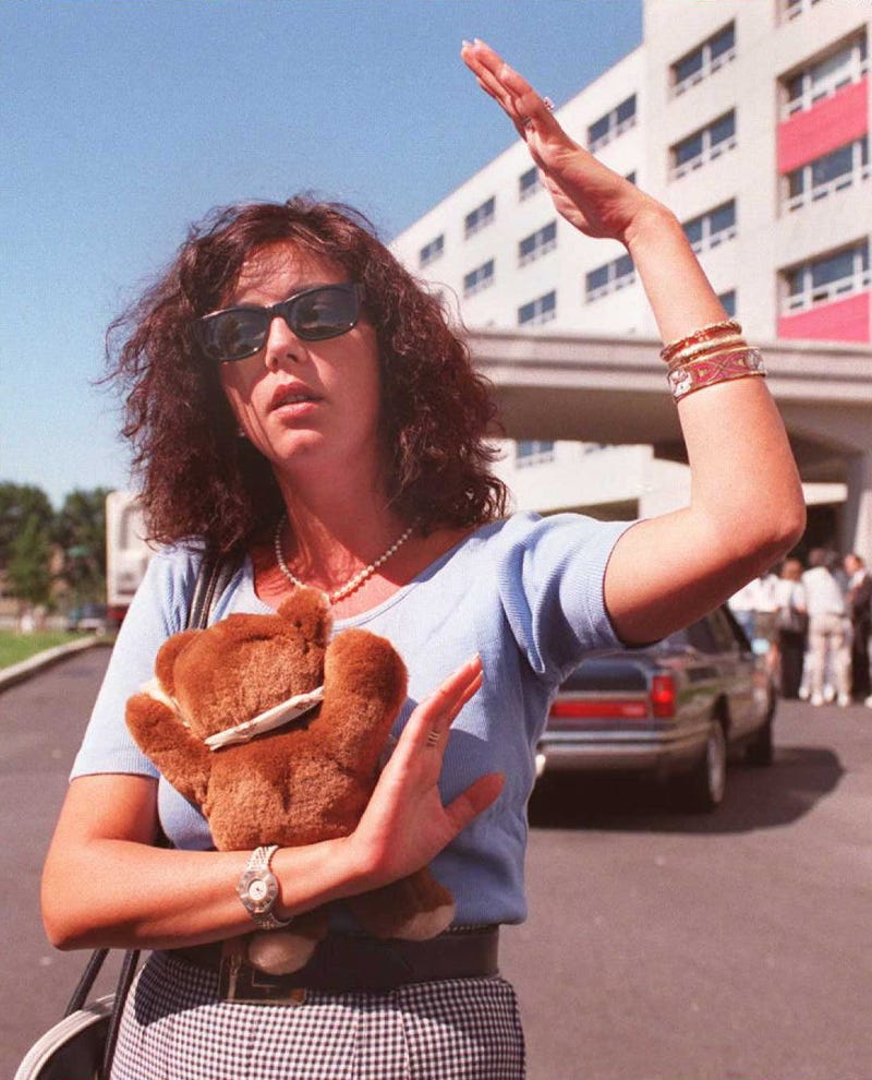 Catherine Cayrol from France, holding a stuffed bear, speaks to reporters 21 July outside the Ramada Inn at Kennedy Airport in New York where families of the victims of TWA flight 800 are staying. Catherine Cayrol's husband, Jacques Cayrol, was on the flight. 