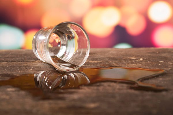 Shot glass of whiskey spilled on a bar
