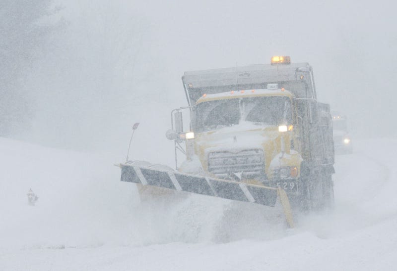 A lone snow plow is barely visible through the wind blown snow as it navigates a highway during a major winter snowstorm.