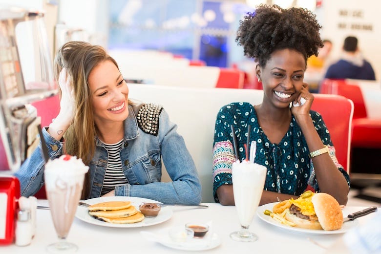 Two friends eating pancakes and a hamburger at a diner