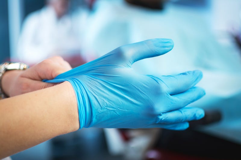 Close up of female doctor's hands putting on blue sterilized surgical gloves in the office.