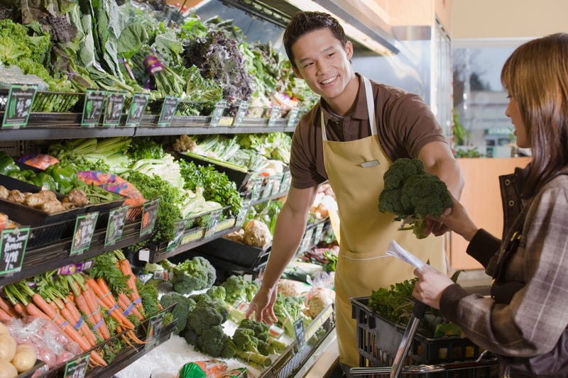 Store employee helping a customers shop for produce at a supermarket.