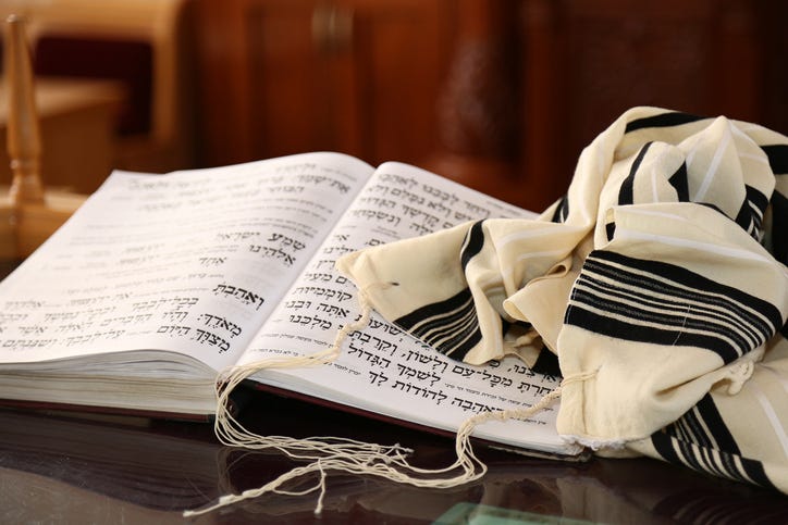 A book of Jewish scripture and a prayer shawl sit on a table.