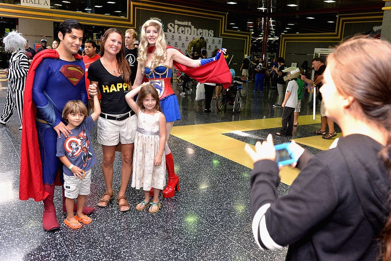 A family posing with people dressed as Superman and Supergirl