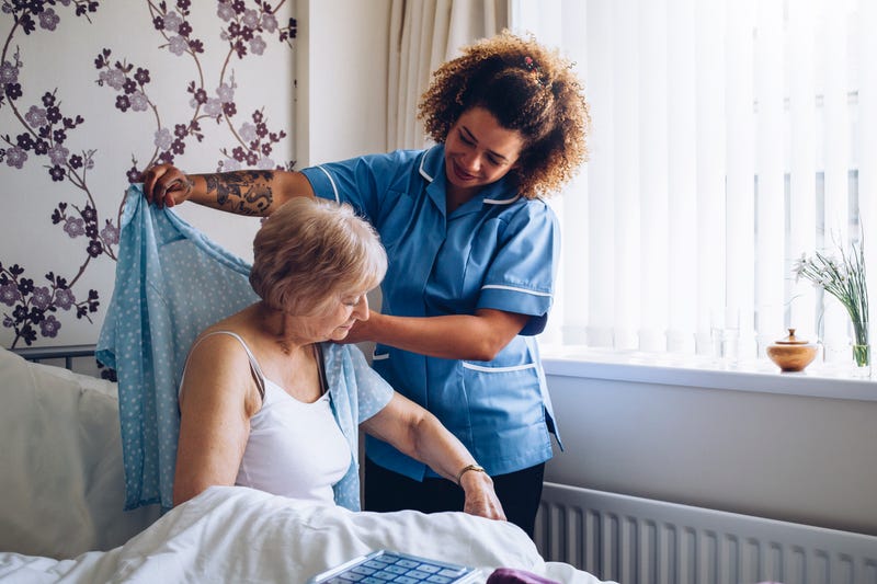 A home caregiver helps a senior woman get dressed.