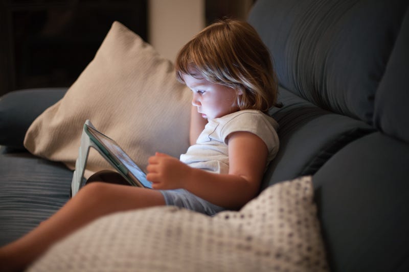 stock image of a young child sitting on a couch and watching something on an ipad