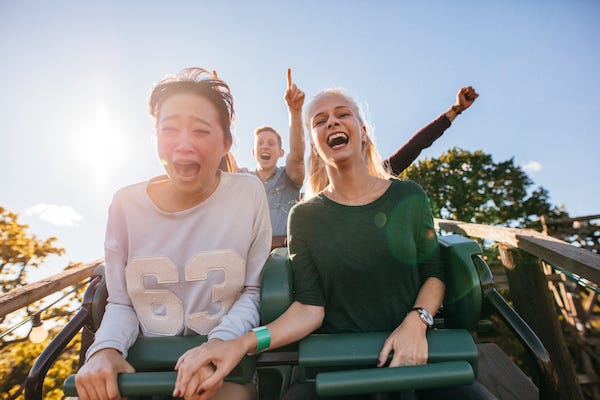 Enthusiastic young friends riding amusement park ride; roller coaster