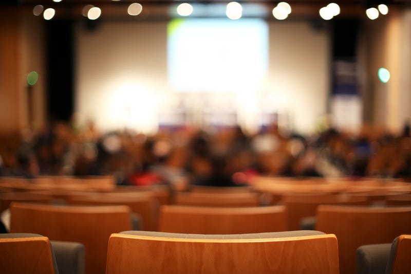 A conference room, with blurred attendees in the background
