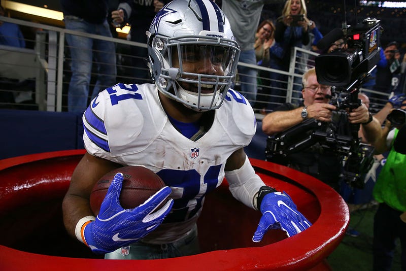 zekiel Elliott #21 of the Dallas Cowboys celebrates after scoring a touchdown by jumping into a Salvation Army red kettle during the second quarter against the Tampa Bay Buccaneers at AT&T Stadium on December 18, 2016 in Arlington, Texas.