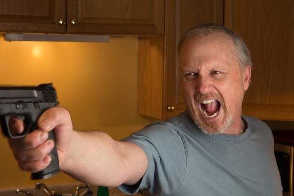 Man with a hostile expression pointing a gun in a kitchen