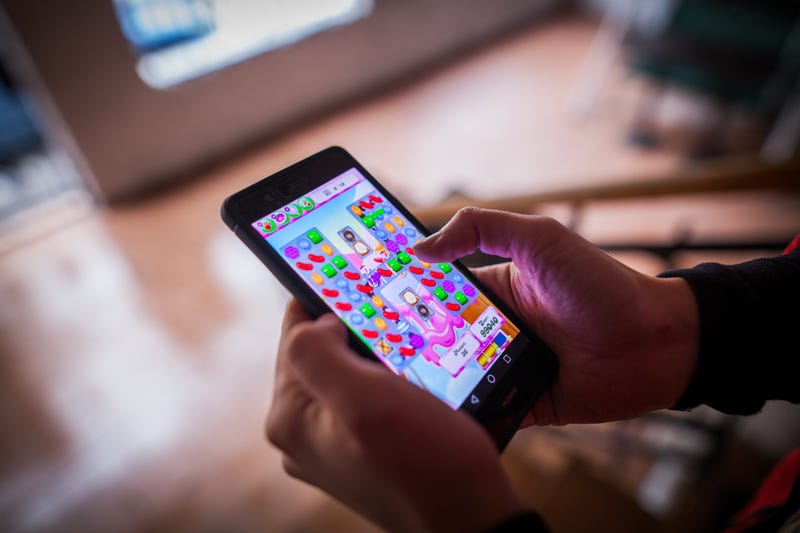 Close up illustrative editorial shot of a person's hands, holding a smartphone and playing Candy Crush Saga game.