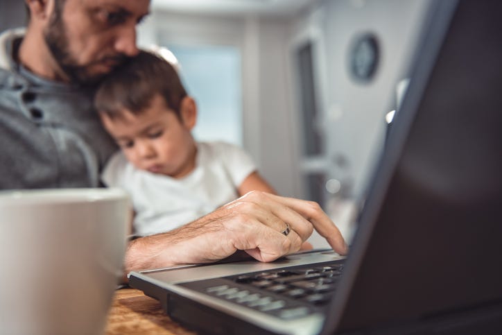 Father working on laptop at home office and holding son on his lap