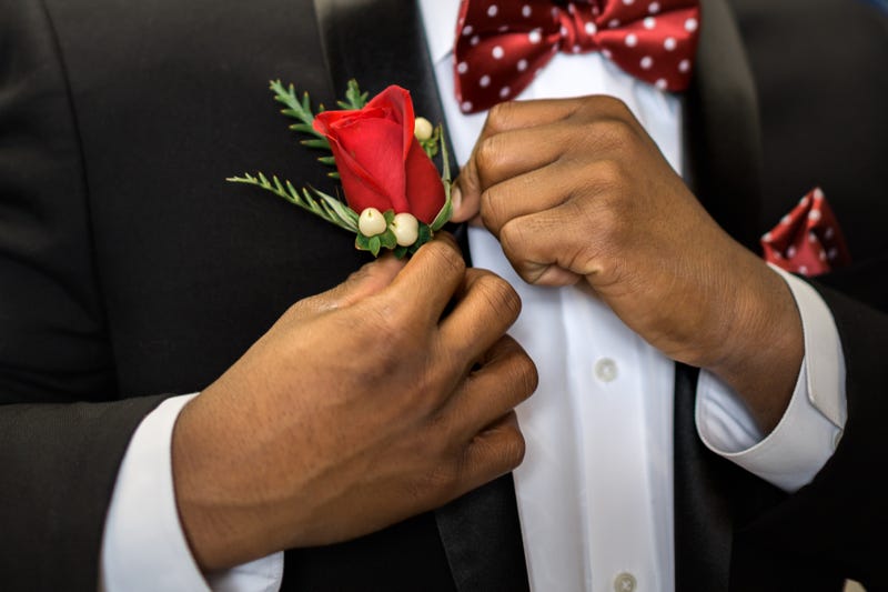 Teen pins his rose boutonniere to formal suit getting dressed and ready for prom