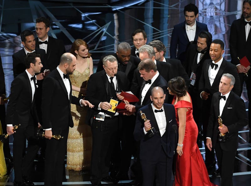 'La La Land' producer Fred Berger (R) speaks at the microphone as production staff and representatives from PricewaterhouseCoopers, Martha L. Ruiz and Brian Cullinan, consult behind him regarding a presentation error of the Best Picture award (later awarded to 'Moonlight') onstage during the 89th Annual Academy Awards at Hollywood & Highland Center on February 26, 2017 in Hollywood, California.