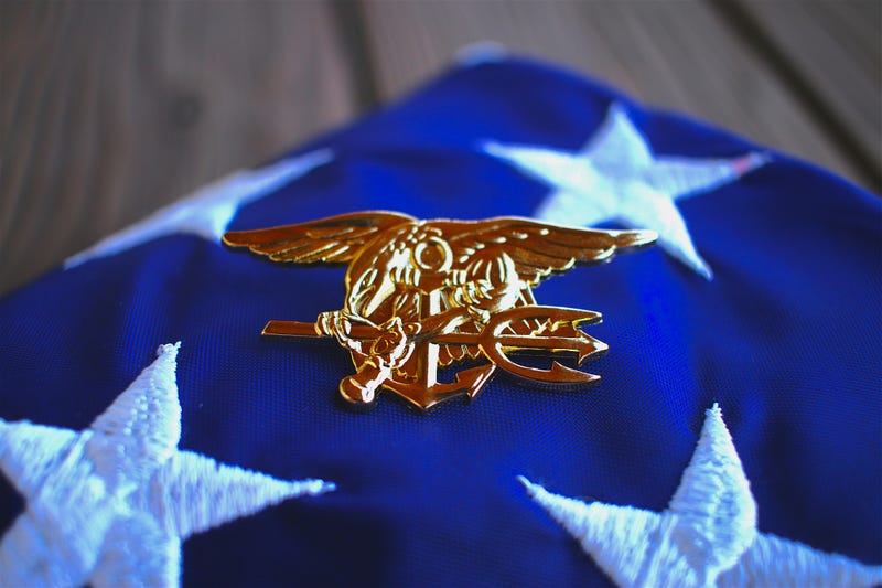 Navy SEAL trident rests atop a folded American flag.