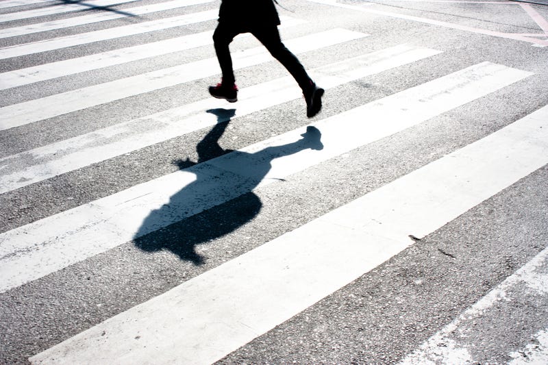 Blurry child's legs and kid's shadow with a backpack, on zebra crossing while running over the street in black and white