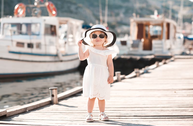 fashionable toddler girl in a dress standing on a boat dock