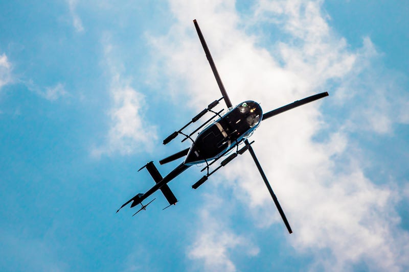 Black helicopter seen flying in blue skies with some clouds.