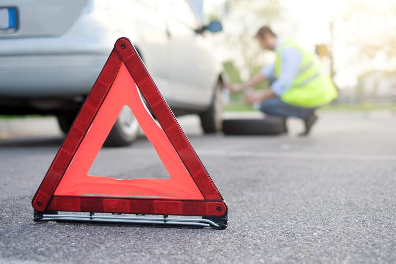 A driver changes a tire on the side of the road.