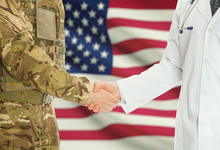 Military man in uniform and doctor shaking hands with U.S. flag in background
