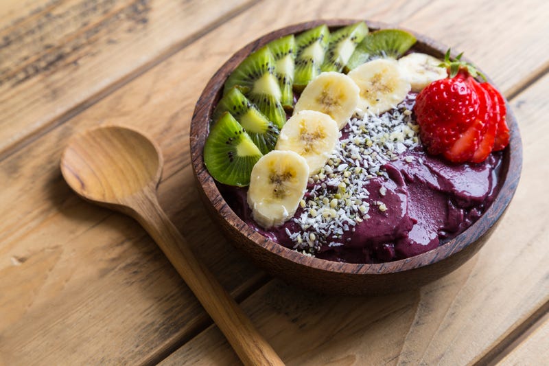 Bowl of acai purée with toppings of banana, kiwi, strawberry and seeds.