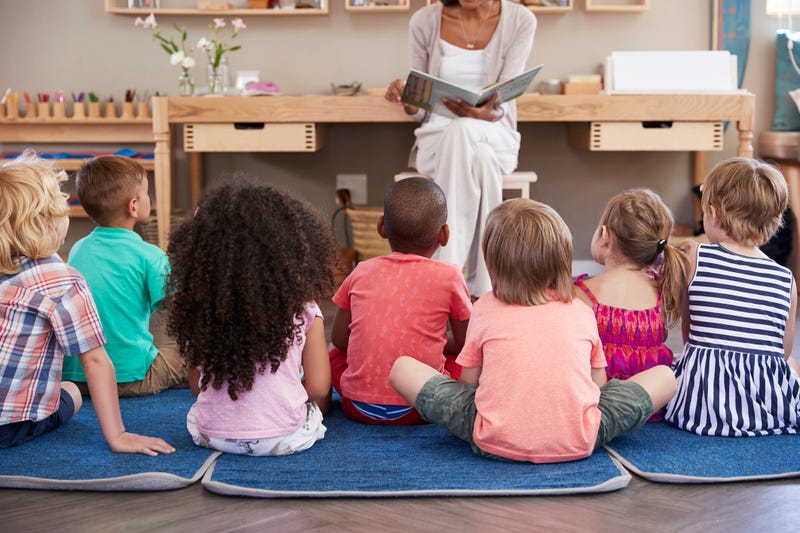 Children sitting on floor in front of a teacher stock photo. 