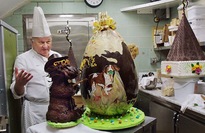 White House Pastry Chef Roland Mesnier present his creation, a 40-pound semi-sweet chocolate Easter Egg decorated with the First Family's pet dogs Barney (L) and Spot in the White House kitchen March 29, 2002 in Washington, DC.
