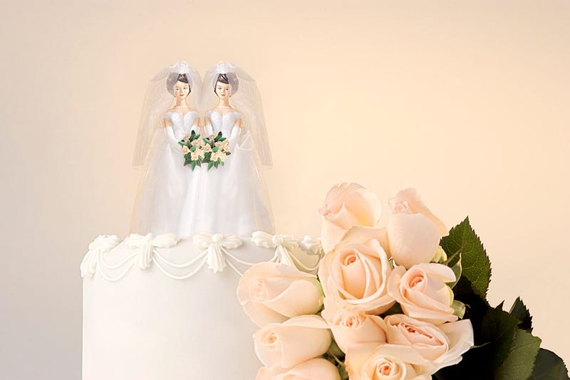 Still life of the top of a wedding cake with two miniature brides cake topper and roses at the side