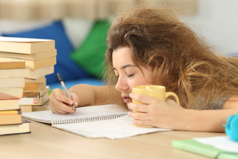 Tired and sleepy student with tousled hair trying to write notes on a desk in her room in a house indoor