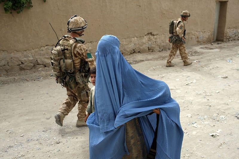 A woman in a burqa and a child walk past two British paratroopers from 3rd Battalion The Parachute Regiment on patrol on June 21, 2008 in Kandahar, Afghanistan
