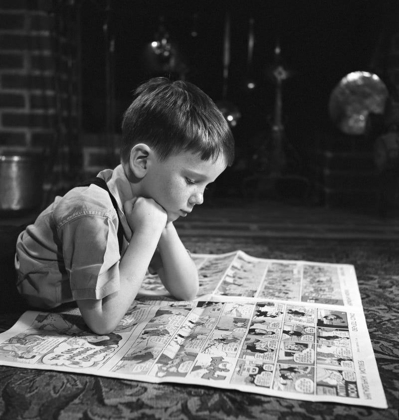 Little boy reading his paper's comic section.
