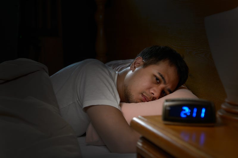 stock photo of man in bed awake with clock that reads 2:11