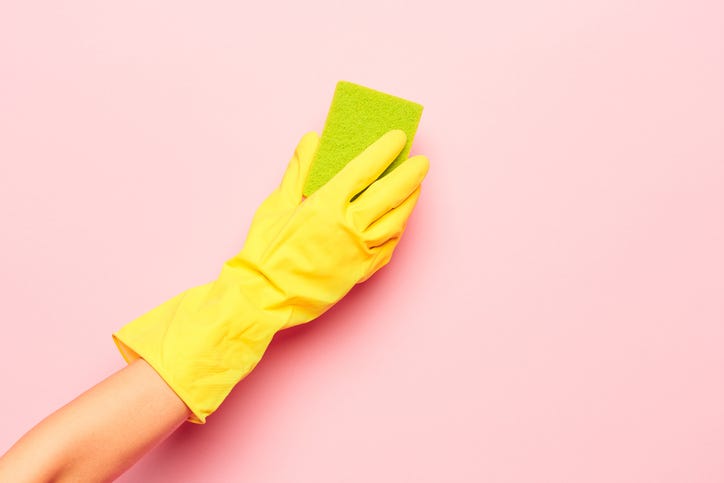 gloved hand cleaning wall with sponge
