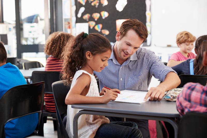 Teacher working with young schoolgirl at her desk in class