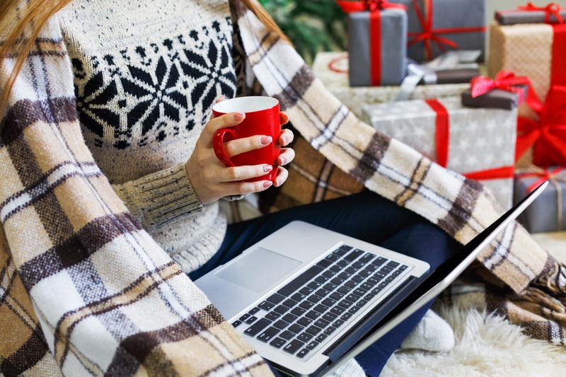 Christmas online shopping. Woman has coffee, buy presents on laptop, prepare to xmas, among gift boxes and packages. Winter sales