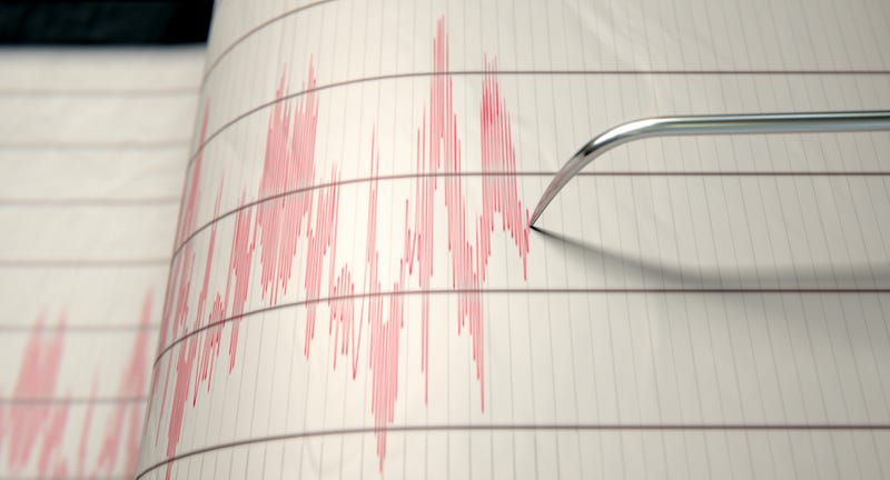 Closeup of a seismograph machine needle drawing a red line on graph paper.