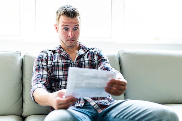 Shocked man holding documents sitting on couch