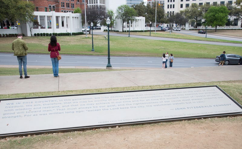 On March 17, 2017, two people pay their respects to John F. Kennedy on the sidewalk above Elm Street in Dealey Plaza, Dallas, Texas. 