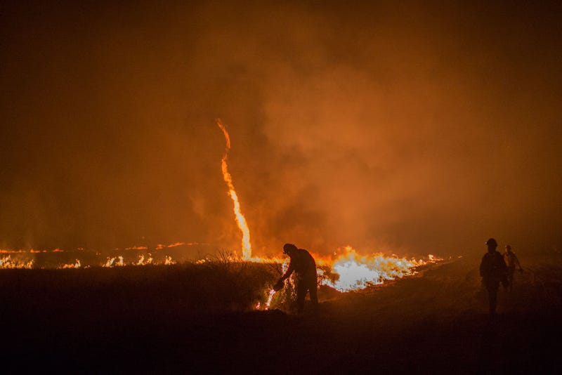 A fire whirl, also called a fire devil, forms as firefighters use drip torches to set a backfire at night in an effort to make progress against the Thomas Fire before the winds return with the daylight near Lake Casitas on December 9, 2017 near Ojai, California. Strong Santa Ana winds have been feeding major wildfires all week, destroying hundreds of houses and forcing tens of thousands of people to stay away from their homes. (Photo by David McNew/Getty Images)