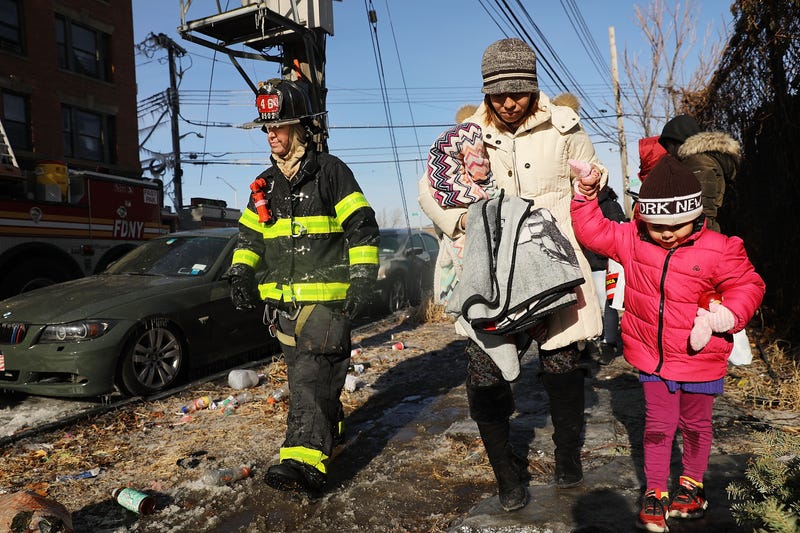 A woman and her child walk outside of their burning building as firefighters battle a 7-alarm fire on January 2, 2018 in the Bronx borough of New York City. The fire, which started around 5:30 a.m. on a frigid Tuesday, is believed to have started on a first-floor furniture store before overtaking the entire building. There were numerous injuries reported from the morning fire which took over 200 firefighters to control.