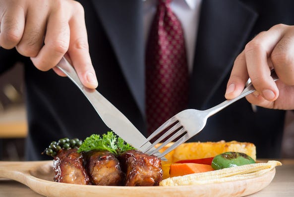 Man in suit and tie cutting steak