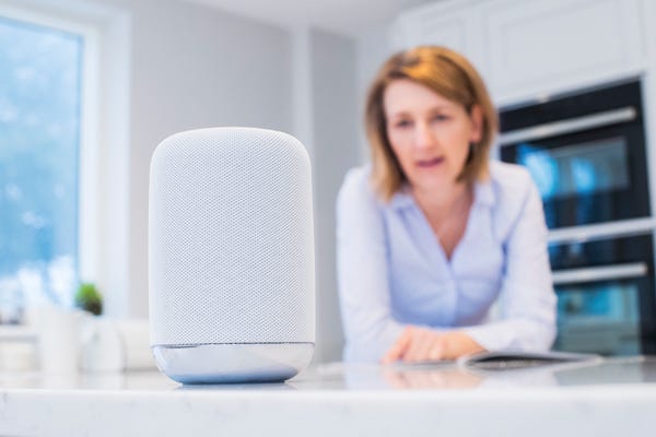 Woman talking to smart speaker device in kitchen