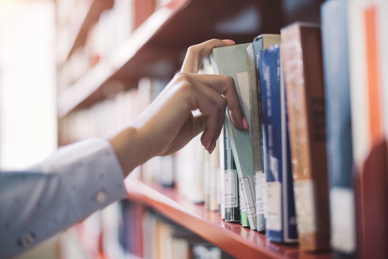 person pulls a book from a library shelf 