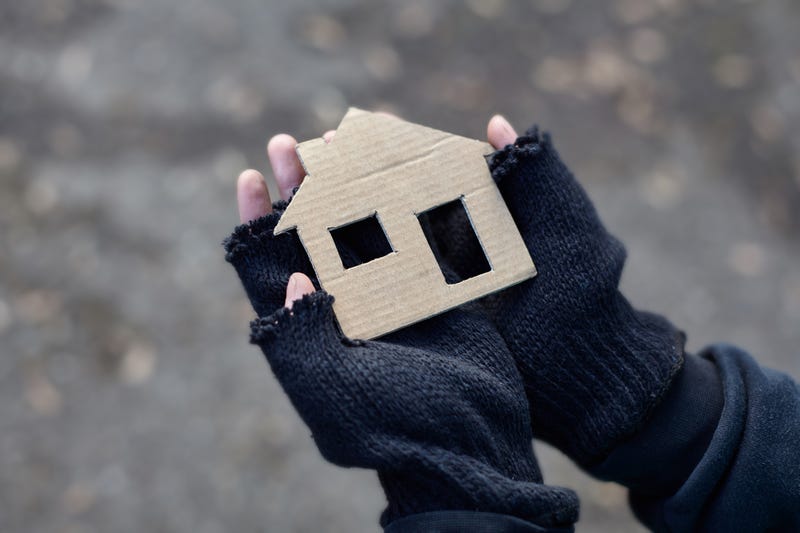 Unhoused child wearing fingerless gloves hold a cardboard cutout of a home.