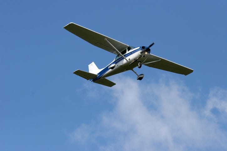 A small Cessna plane soars through the blue sky.