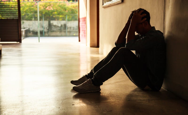A stressed and sad young man sits holding head in hands.