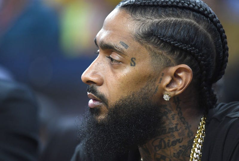 Nipsey Hussle sitting at courtside, looks on during an NBA basketball in Oakland, Calif. in 2018.